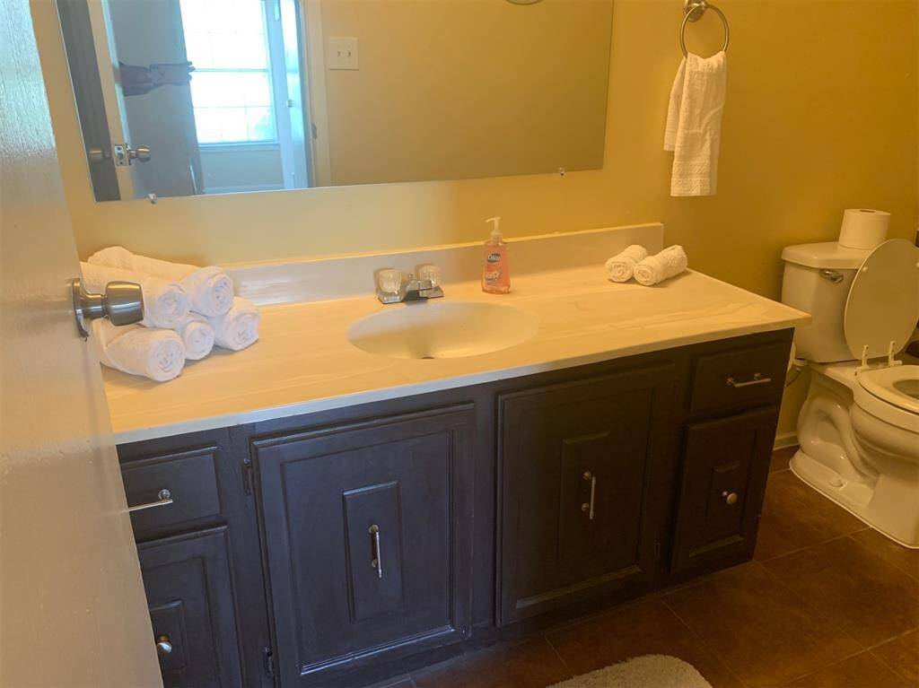 This bathroom features a dark wood vanity with ample storage, a clean countertop with a single sink, and a large mirror. The space is well-lit and includes a standard toilet and towel rack.