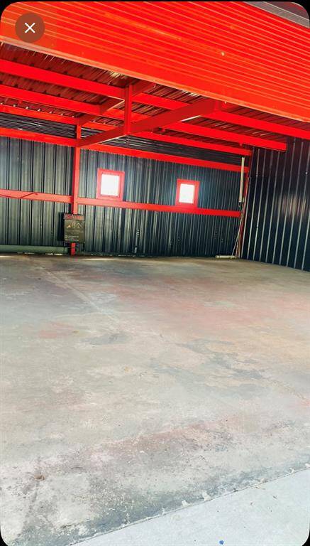 Spacious garage or workshop featuring a durable concrete floor and striking red steel beams. Dark metal-paneled walls and two small windows provide natural light, making it ideal for storage or a workspace.