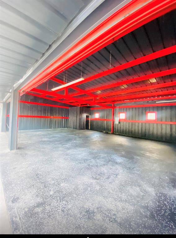 Discover a spacious garage or workshop with a sleek industrial vibe, featuring striking black walls and ceilings contrasted by bold red beams. The durable concrete floor is perfect for versatile use.