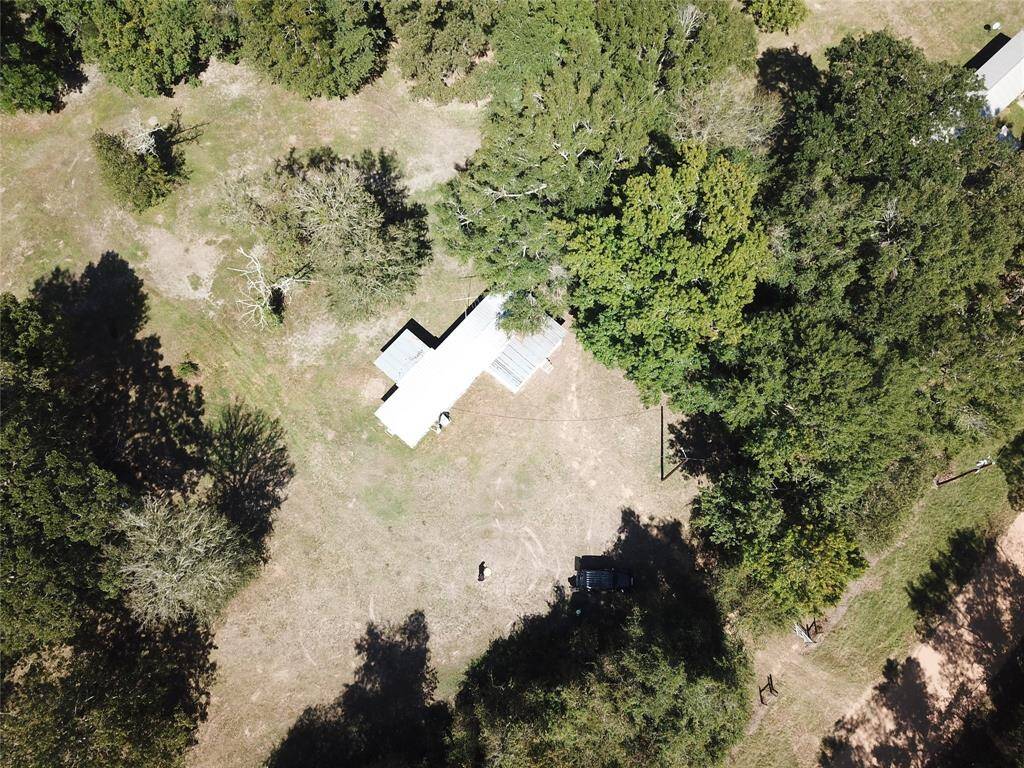 Aerial view of a rural property with a building surrounded by trees and open land, casting long shadows on the ground.