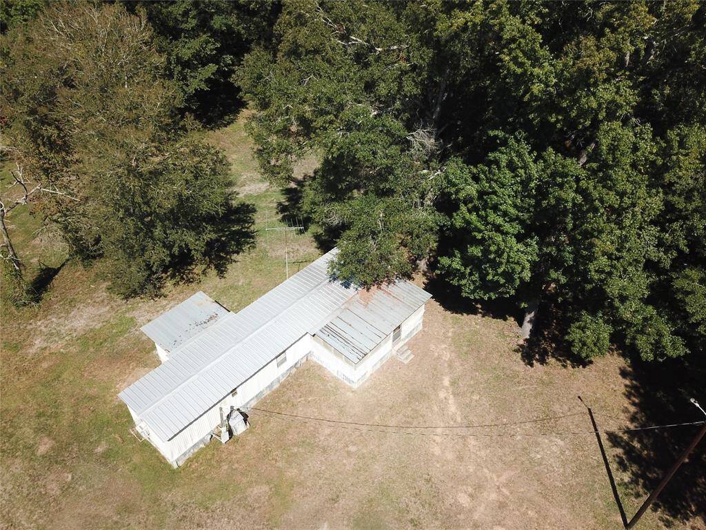 Aerial view of a small, isolated metal-roofed building surrounded by trees with a clearing that shows pathways or utility lines.