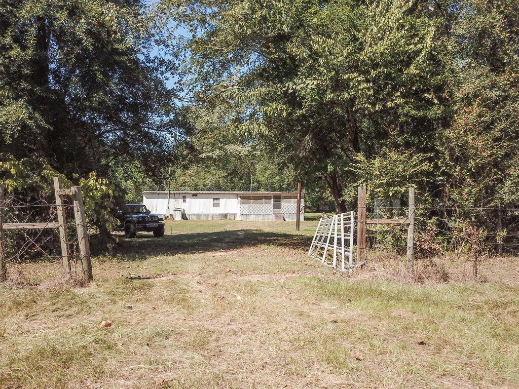Rural landscape with a wooden fence, a white ladder on the ground, trees, and a building with a truck parked beside it.