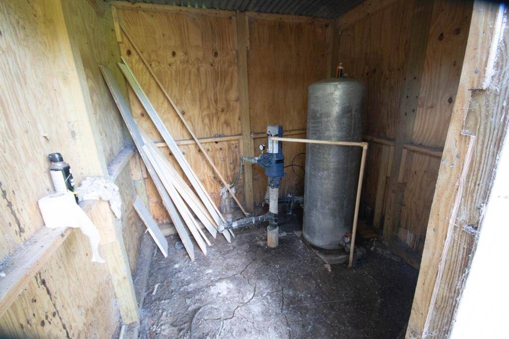 A rustic wooden shed interior with a water pump system, storage tank, and assorted construction materials  leaning against the wall.