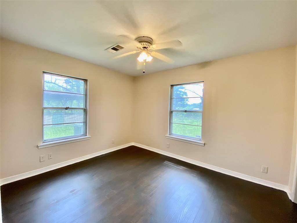 Bedroom features neutral walls, dark hardwood floors, two large windows providing ample natural light, and a ceiling fan. It appears spacious and well-lit, ideal for a variety of layouts.