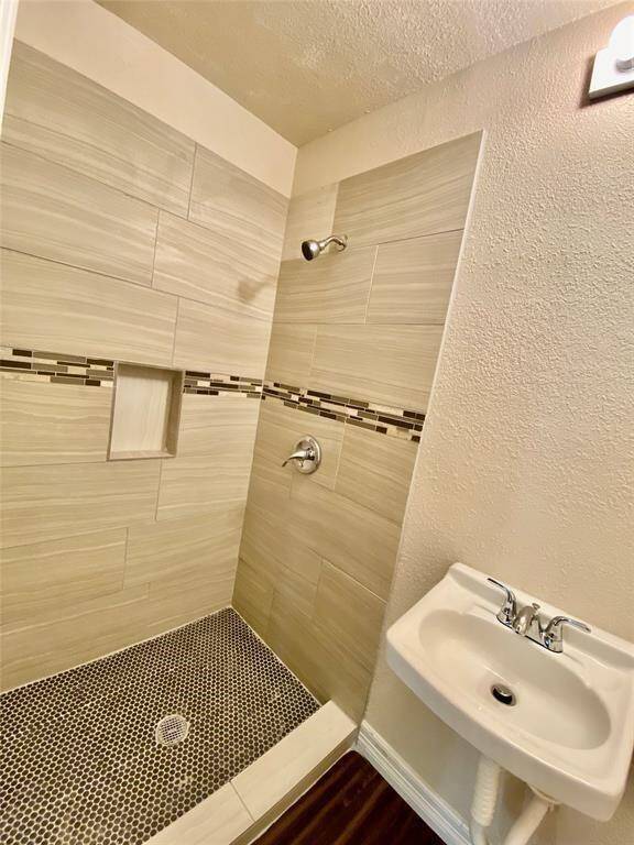 Second  bathroom featuring a walk-in shower with beige tiling and a decorative mosaic accent strip. It includes a small white pedestal sink with chrome fixtures and a built-in niche for shower essentials. The floor of the shower has a black and white pebble tile design.