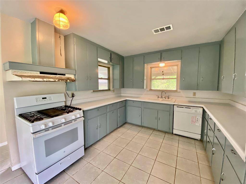 Good size kitchen features pale blue cabinetry, white appliances, tile flooring, and a window over the sink for natural light.