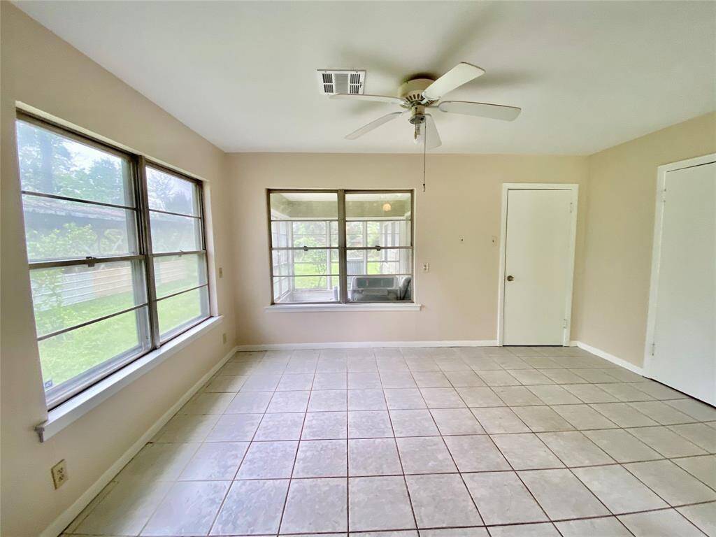 This is a bright, empty room with tiled flooring, multiple windows providing natural light, and a ceiling fan. It appears to be ready for move-in.