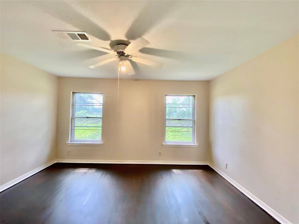 Bright dining room featuring glossy dark wood floors, a neutral wall color, two windows providing natural light, and a ceiling fan with lighting.
