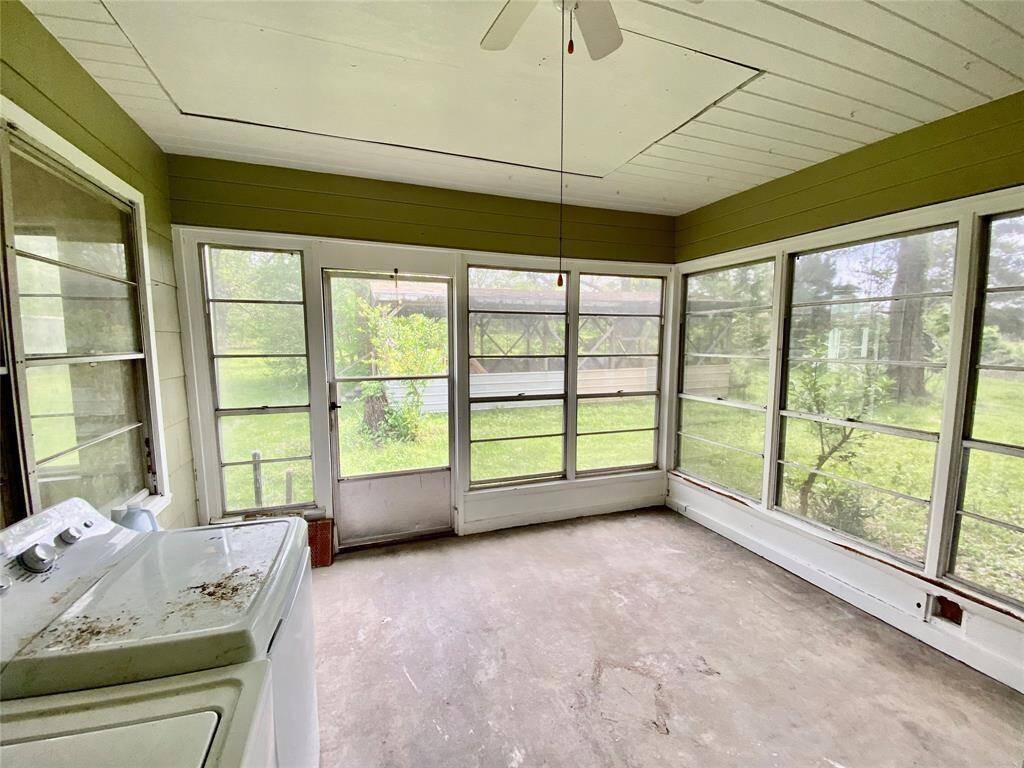 Large sunroom with ample natural light from wall-to-wall windows, overlooking a green backyard. The room appears to need some cleaning and possibly updating, but has great potential as a relaxing space or entertaining area.