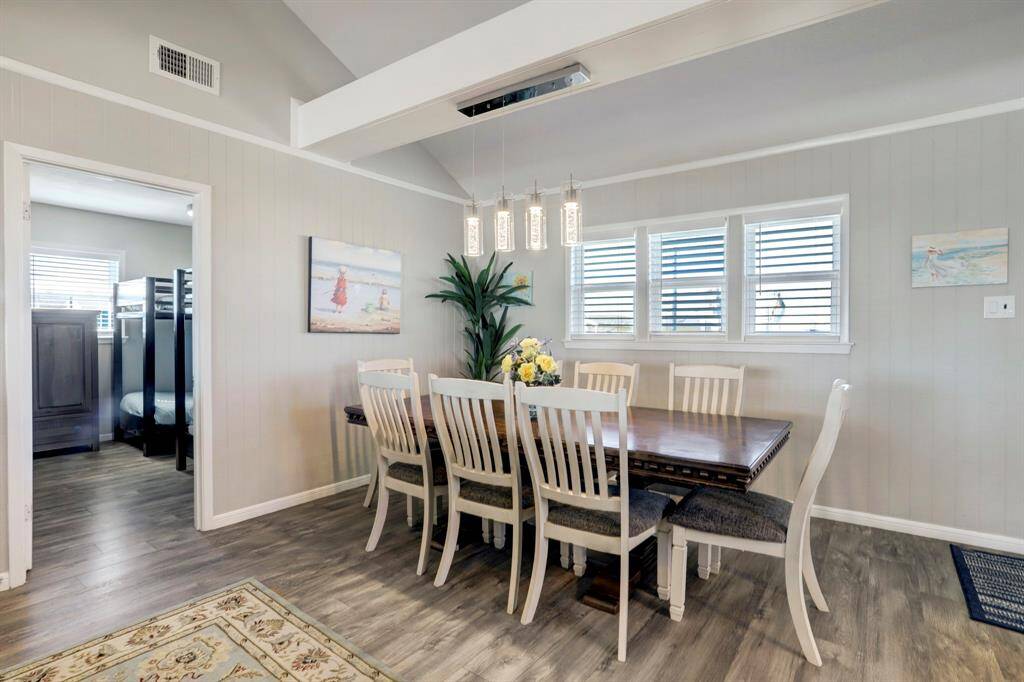 This dining area features a modern, cozy design with a wooden table and chairs, complemented by stylish pendant lighting. The space is brightened by natural light through the windows, and the adjacent room offers additional living space.