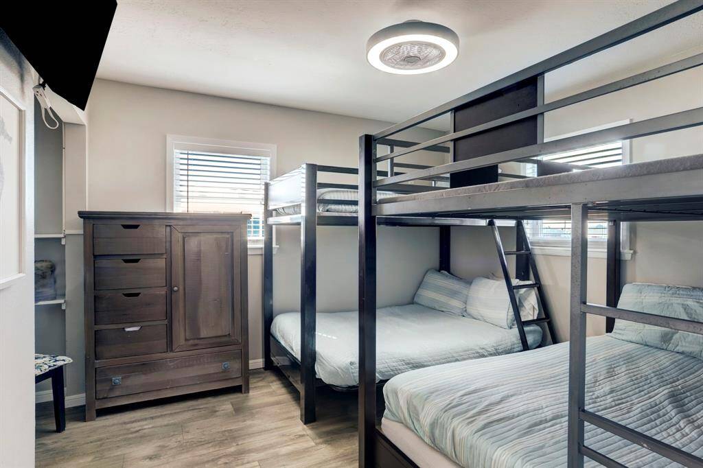 This bedroom features two bunk beds with a modern design, accommodating multiple sleepers. It has a sleek dresser, wood flooring, and ample natural light from a window, creating a cozy and functional space.