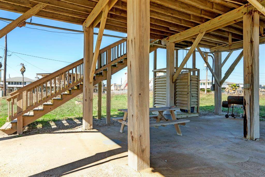 This photo showcases the understructure of a raised home, featuring wooden support beams, a staircase, an outdoor shower, and a picnic table, ideal for coastal or flood-prone areas.