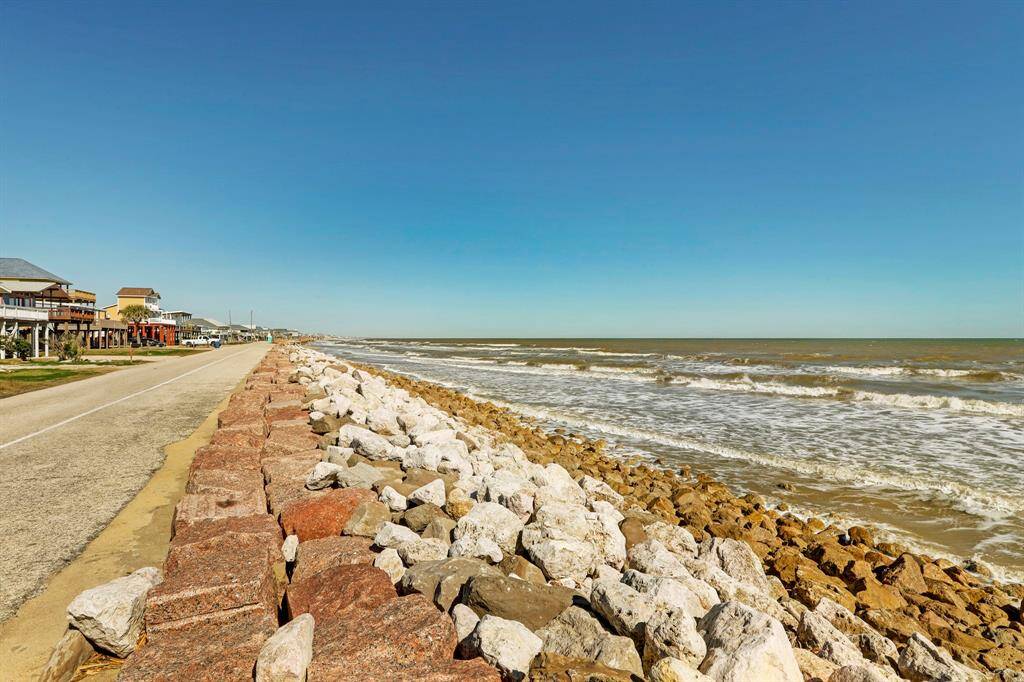 Scenic coastal view showcasing a charming beachfront road lined with houses on one side and a rocky shoreline leading to the ocean on the other. Ideal for those seeking a picturesque seaside living experience.