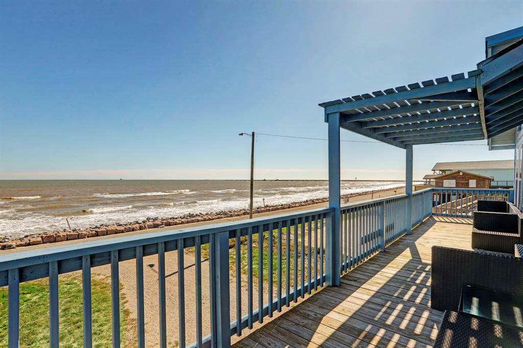 This photo showcases a home with a spacious wooden deck overlooking a serene beachfront. The deck features partial covering and comfortable seating, perfect for enjoying ocean views and coastal breezes.