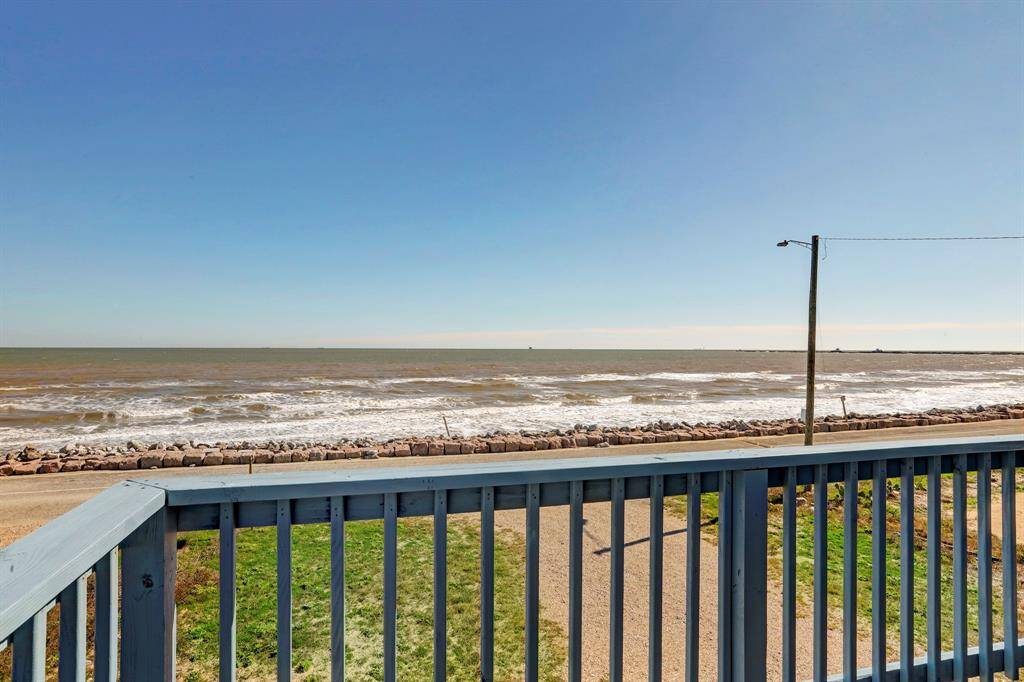 This photo showcases a coastal view from a balcony, featuring a clear blue sky and ocean waves gently crashing onto a rocky shoreline, perfect for enjoying serene seaside living.