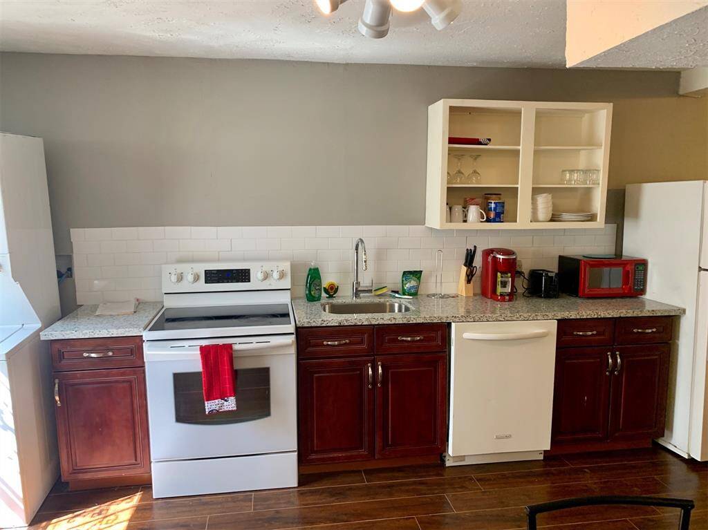 This is a cozy kitchen featuring modern appliances, granite countertops, white subway tile backsplash, and rich wooden cabinetry. The space is well-lit with natural lighting complementing the warm color palette.