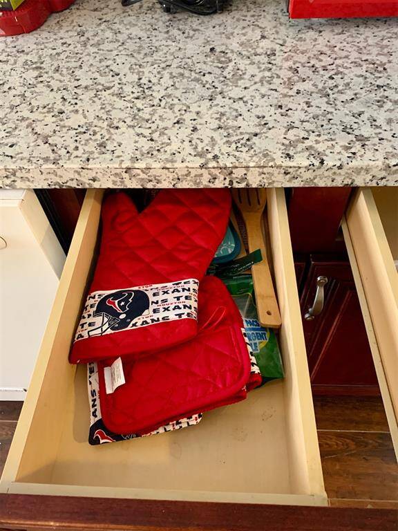 You're looking at a kitchen drawer under a granite countertop, partially open to reveal oven mitts and some kitchen utensils. The cabinetry has a classic design with a neutral color palette.
