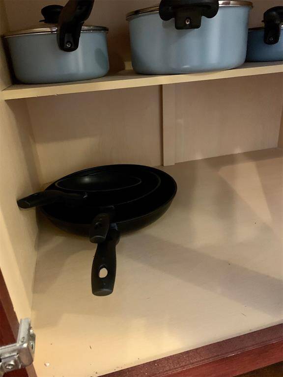 The photo shows a tidy kitchen cabinet with neatly arranged cookware, featuring a set of blue pots with lids and a black frying pan. The cabinet offers practical storage space for kitchen essentials.
