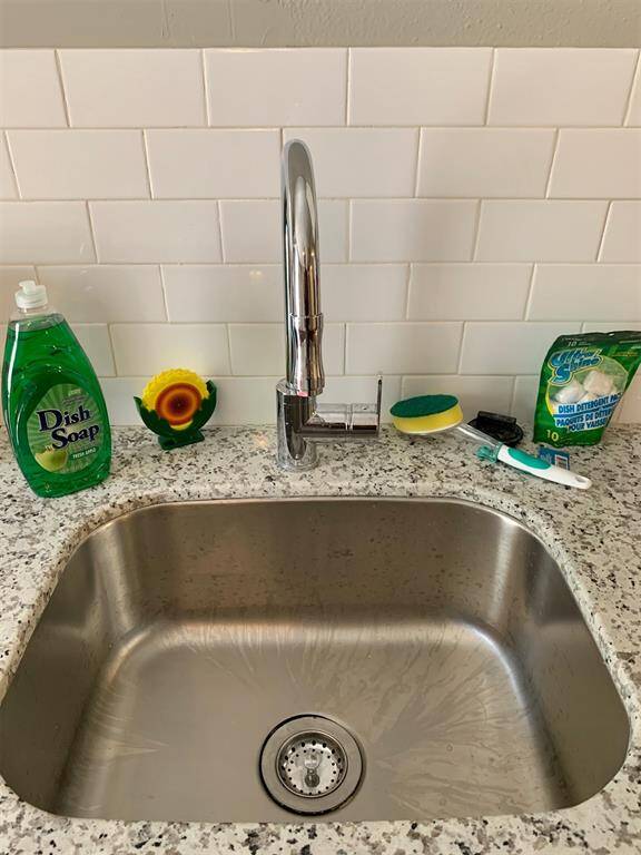 This photo shows a modern kitchen sink with a sleek stainless steel finish, complemented by white subway tile backsplash. The area is neatly organized with dish cleaning essentials on the countertop.