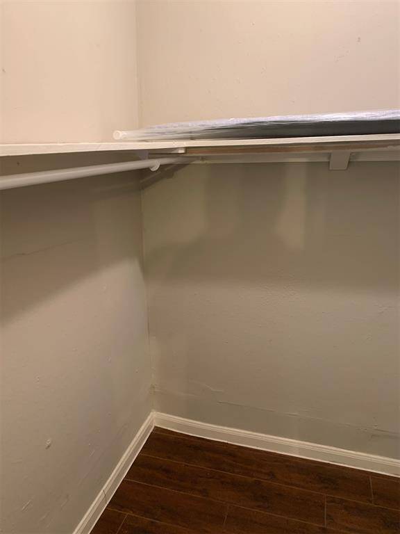 The photo shows a small, empty closet space with a single shelf and hanging rod, featuring beige walls and a dark wood floor.