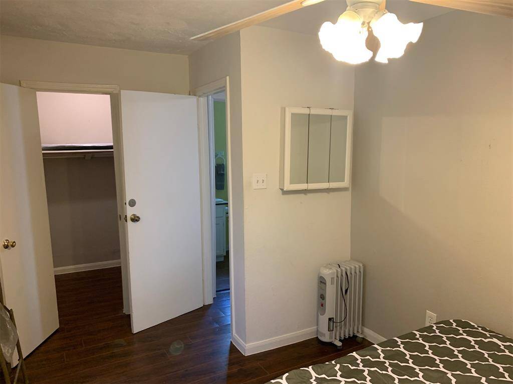 This is a clean, well-lit room with hardwood floors, featuring a closet, an attached bathroom, and a built-in medicine cabinet. A portable radiator provides additional heating.