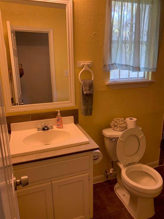 This is a cozy bathroom featuring a single vanity with a cabinet, a mirror, a toilet, and a window providing natural light. The walls are painted in a warm yellow tone.