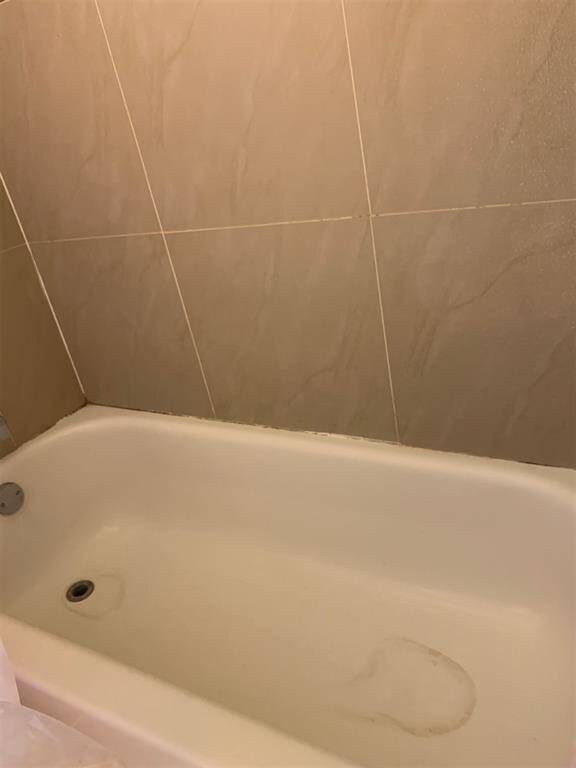 The photo shows a standard white bathtub with beige wall tiles. The tub appears to have some wear and staining that may require cleaning or refinishing.