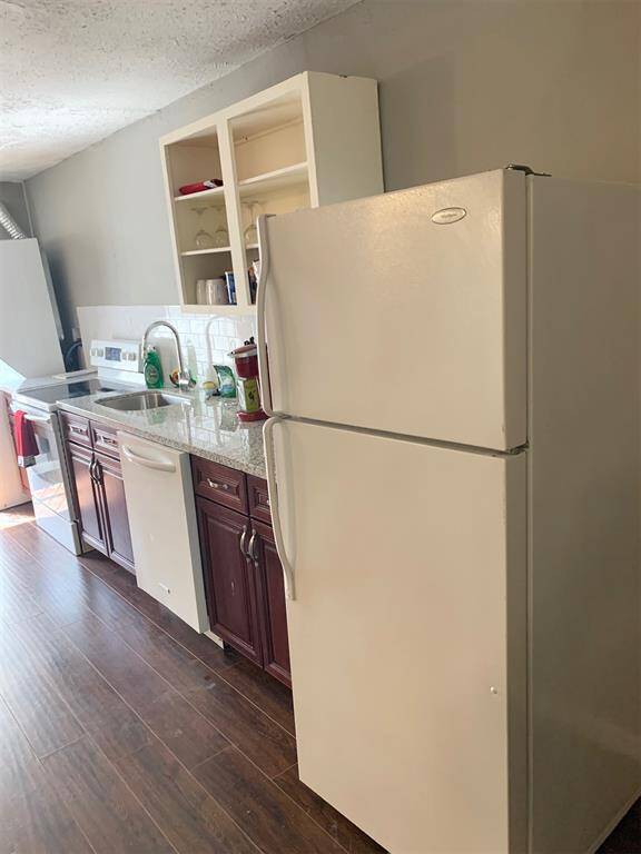 This is a compact kitchen with modern appliances, dark wood cabinetry, and a tile backsplash. The space has laminate flooring and seems well-maintained.