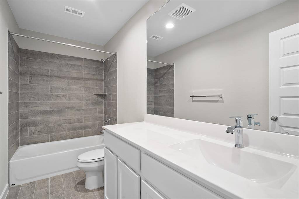 Secondary bath features tile flooring, bath/shower combo with tile surround, white stained wood cabinets, beautiful light countertops, mirror, sleek fixtures and modern finishes.
