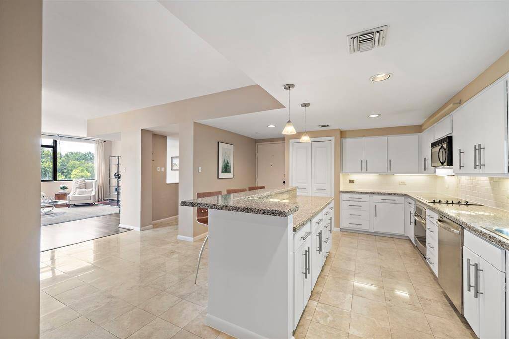 Prepare and serve meals with ease in the open kitchen, equipped with a stainless steel cooktop and oven, granite countertops, and a spacious island.