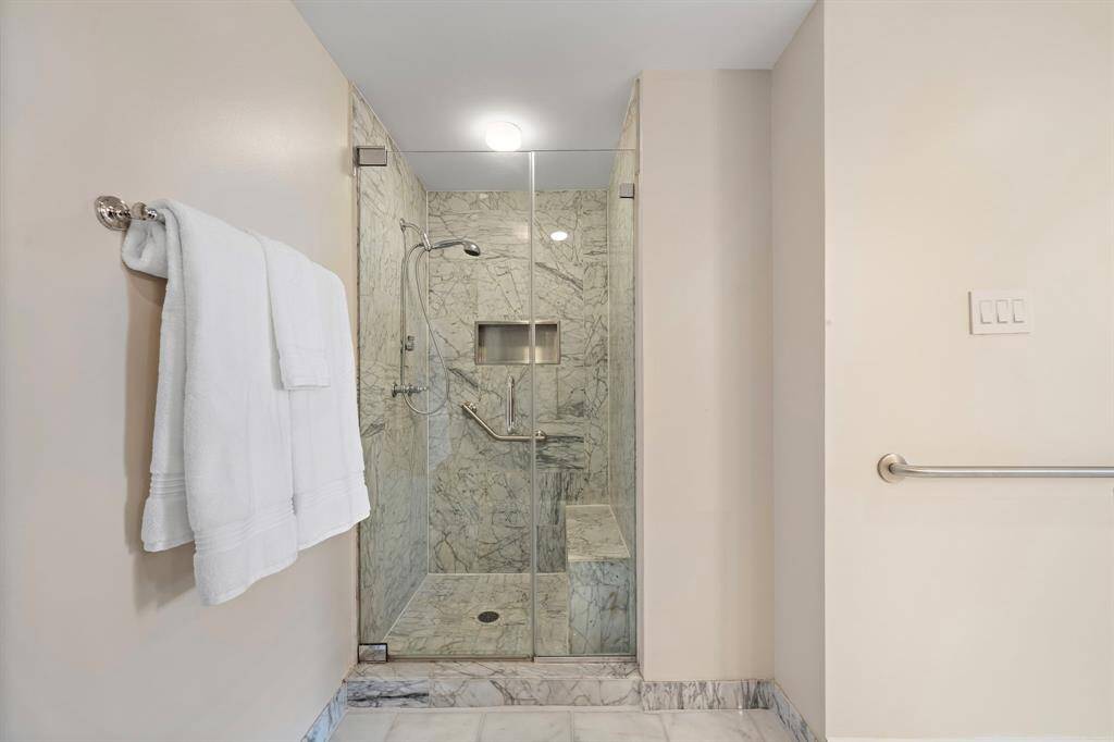 The glass-enclosed shower is adorned with marble tiling and fitted with both a built-in shower bench and a niche for added convenience.