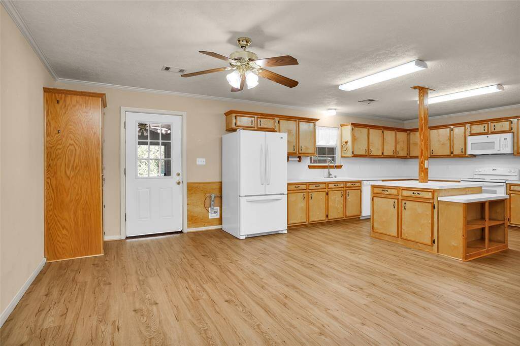 This spacious kitchen features ample wooden cabinetry, a central island, and modern appliances. It has a ceiling fan, wood-style flooring, and a door leading outside, offering both functionality and convenience.