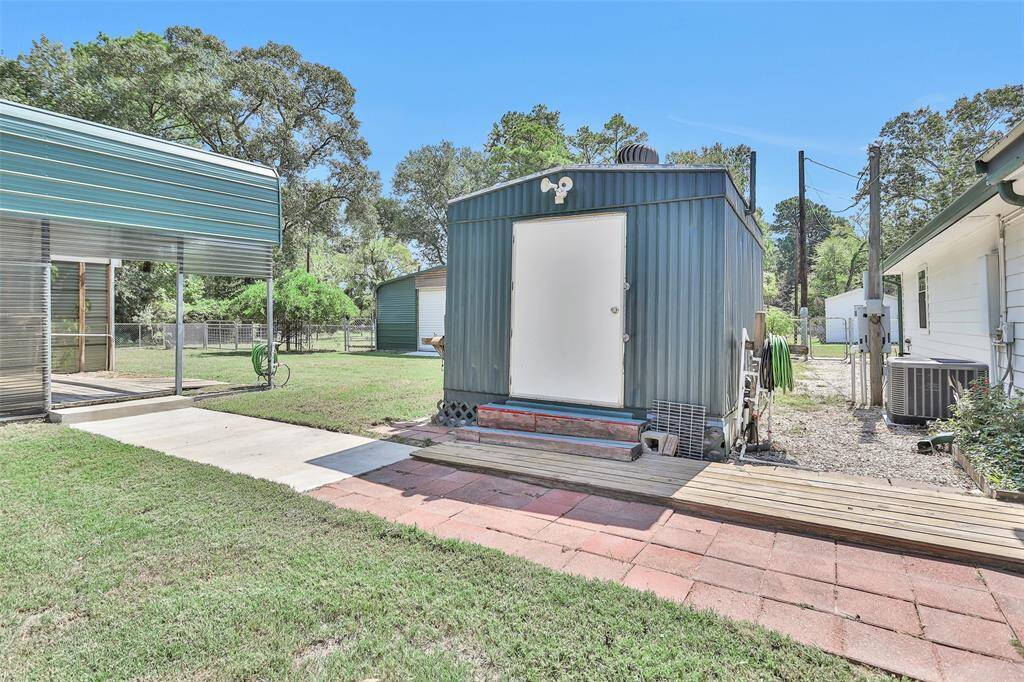 This convenient half bath and utility shed, located just behind the house, features a water softener, its own water heater, a sink, shelves, and a toilet.