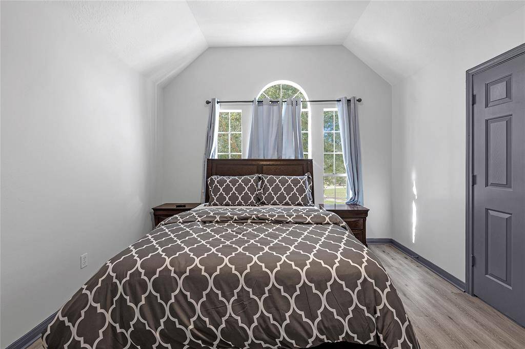 This cozy bedroom features vaulted ceilings, a large arched window for natural light, and a stylish modern design with neutral tones, creating a welcoming atmosphere.
