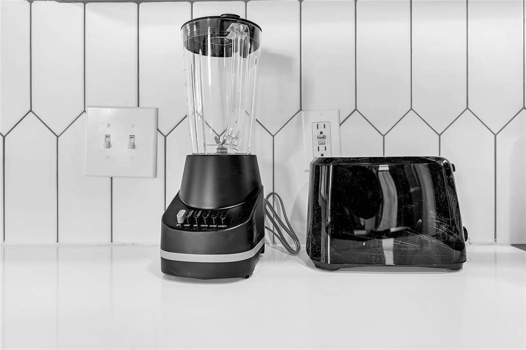 This kitchen features a modern backsplash with a white geometric tile design, complemented by a sleek countertop. It includes essential appliances like a blender and toaster, providing a stylish and functional space for meal preparation.