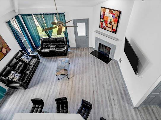 This spacious living room features modern flooring, a cozy fireplace, and abundant natural light from large windows. It includes comfortable seating, a ceiling fan, and stylish decor, offering a welcoming and contemporary atmosphere.