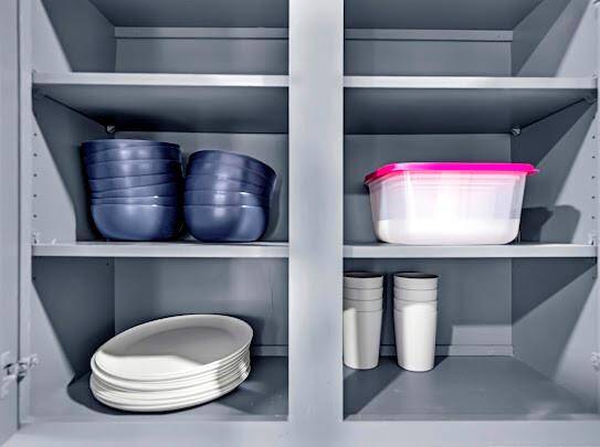 This photo shows a neatly organized kitchen cabinet with shelves holding stacks of bowls and plates, a container, and cups. The cabinet appears spacious and functional for storage.