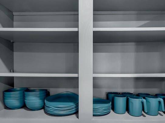 This photo shows a well-organized kitchen cabinet with open shelving, featuring neatly stacked blue dishware and mugs.