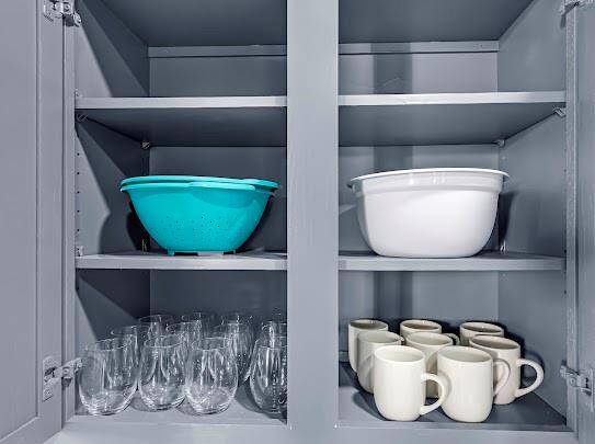 This kitchen cabinet features spacious shelving, neatly organized with glassware, mugs, and bowls, showcasing ample storage for kitchen essentials.