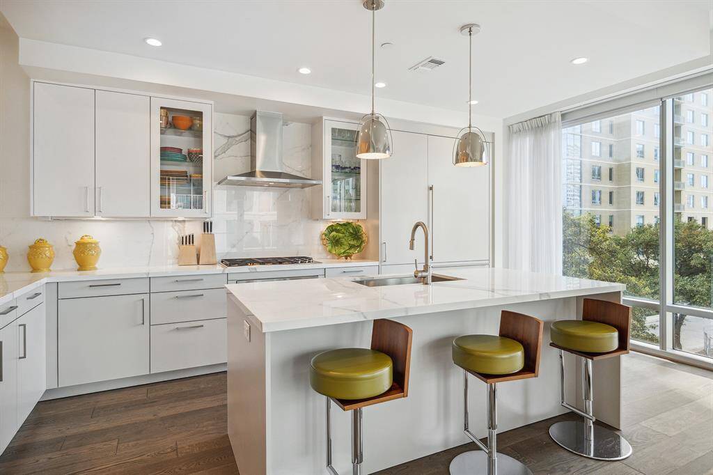 Chef's kitchen with SubZero refrigerator and dishwasher with matching cabinet panels, stainless microwave and under cabinet built-in dual zone stainless wine refrigerator, Wolf stainless 5-burner gas cooktop. Breakfast bar island features Kohler sink with Blanco stainless pull down faucet/spray. Polished porcelain countertops and backsplash throughout. Under cabinet countertop lighting, European-styled SieMatic self-closing drawers and cabinetry in white matte laminate offers 2 glass panel display cabinets.