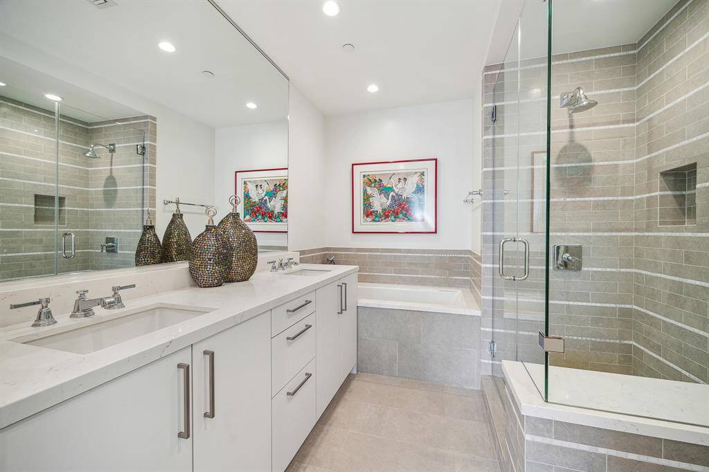 Primary bedroom en suite bath features soaking tub, separate seamless glass shower, dual sinks with neutral tiles, gleaming porcelain floors and countertops. Lutron lights turn on/off automatically upon entry and exit.
