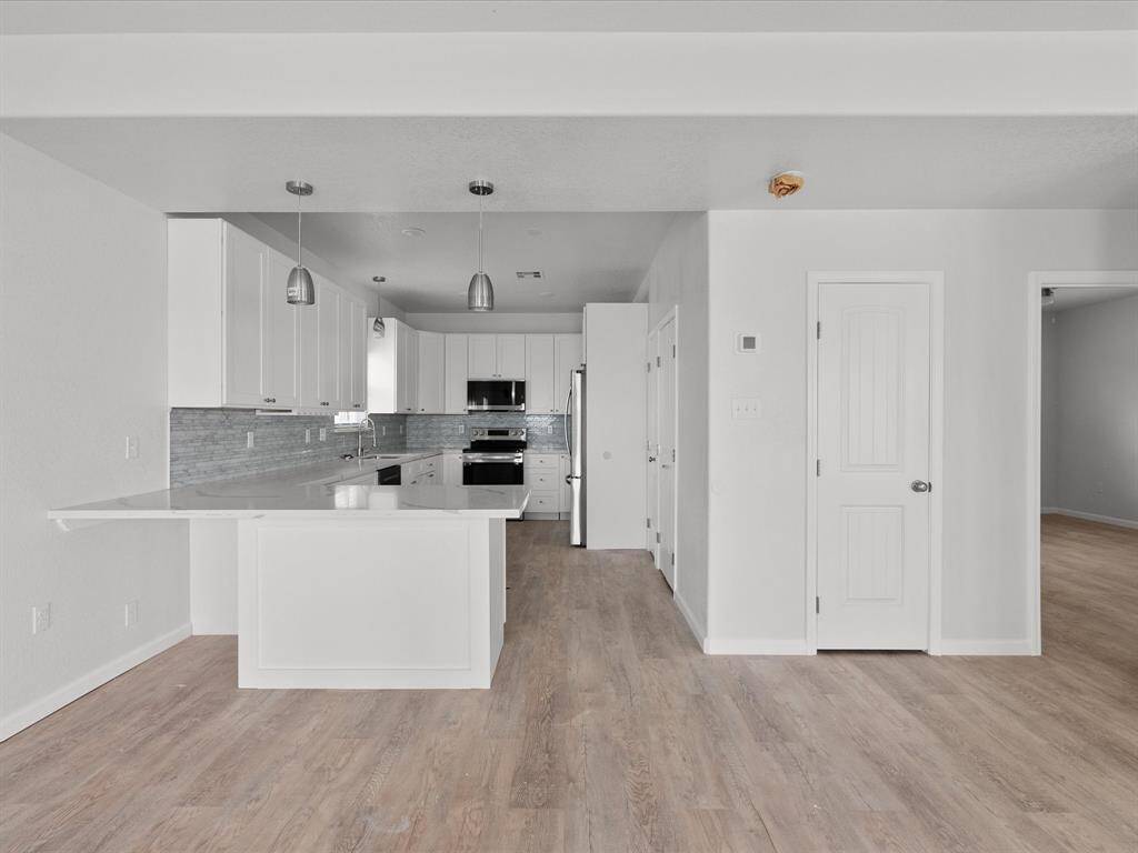This photo showcases a modern, open kitchen with light wood flooring, white cabinetry, and a spacious island. Stainless steel appliances and pendant lighting add to the contemporary feel.