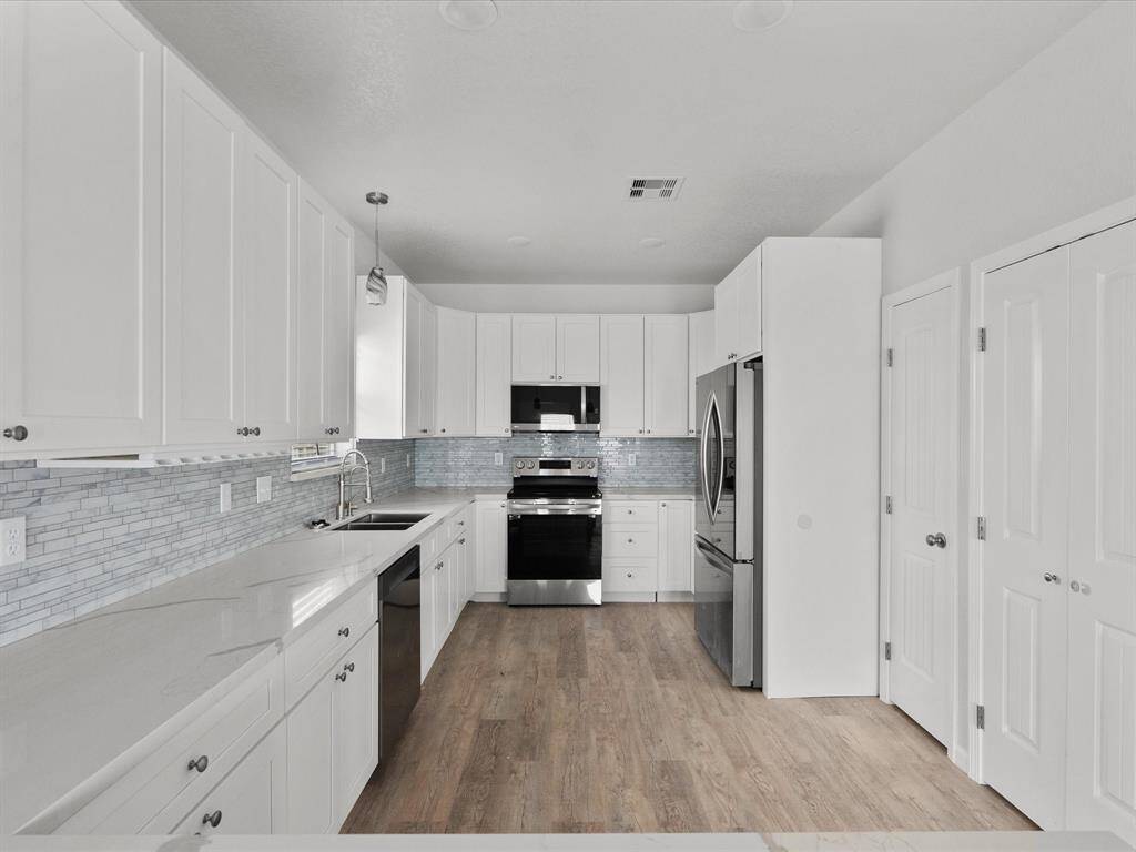 This kitchen features modern stainless steel appliances, sleek white cabinetry, a stylish tile backsplash, and durable wood-look flooring, creating a bright and inviting space.