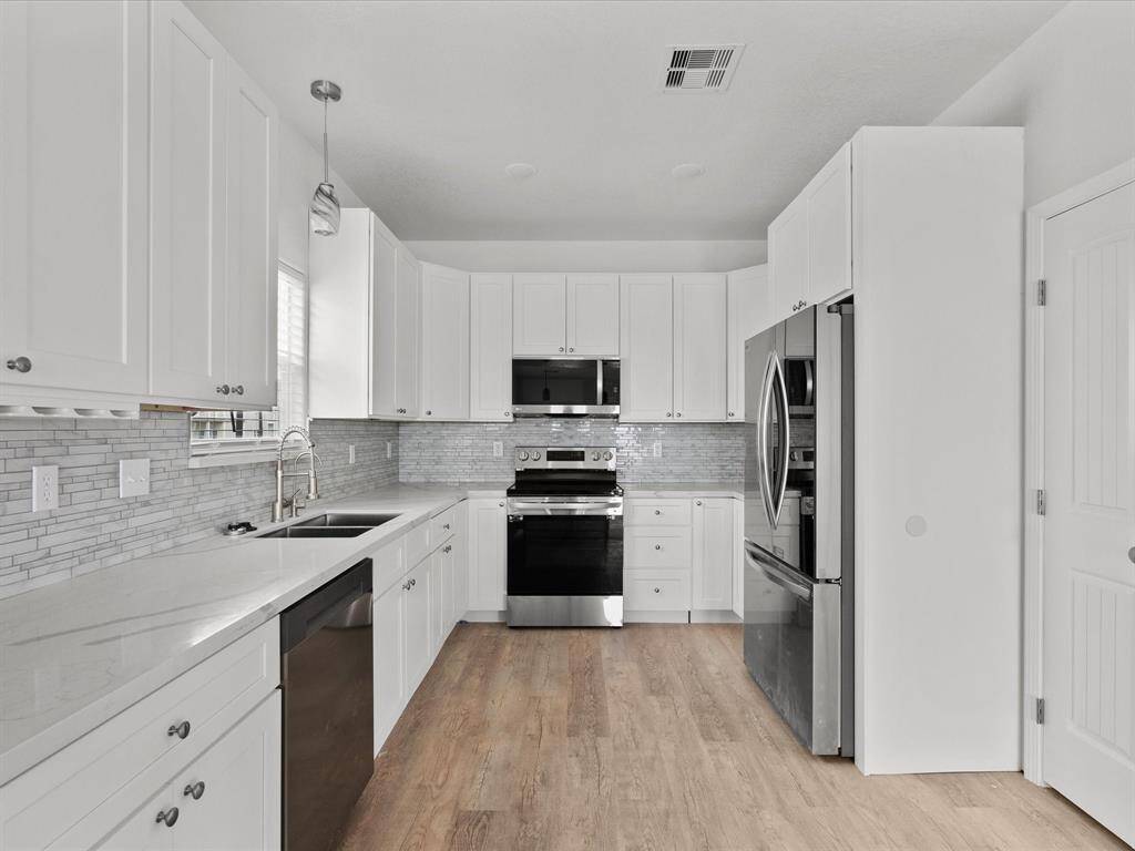 This modern kitchen features sleek white cabinetry, stainless steel appliances, and a stylish gray tile backsplash. It has ample counter space and natural light, with wood flooring adding warmth to the contemporary design.
