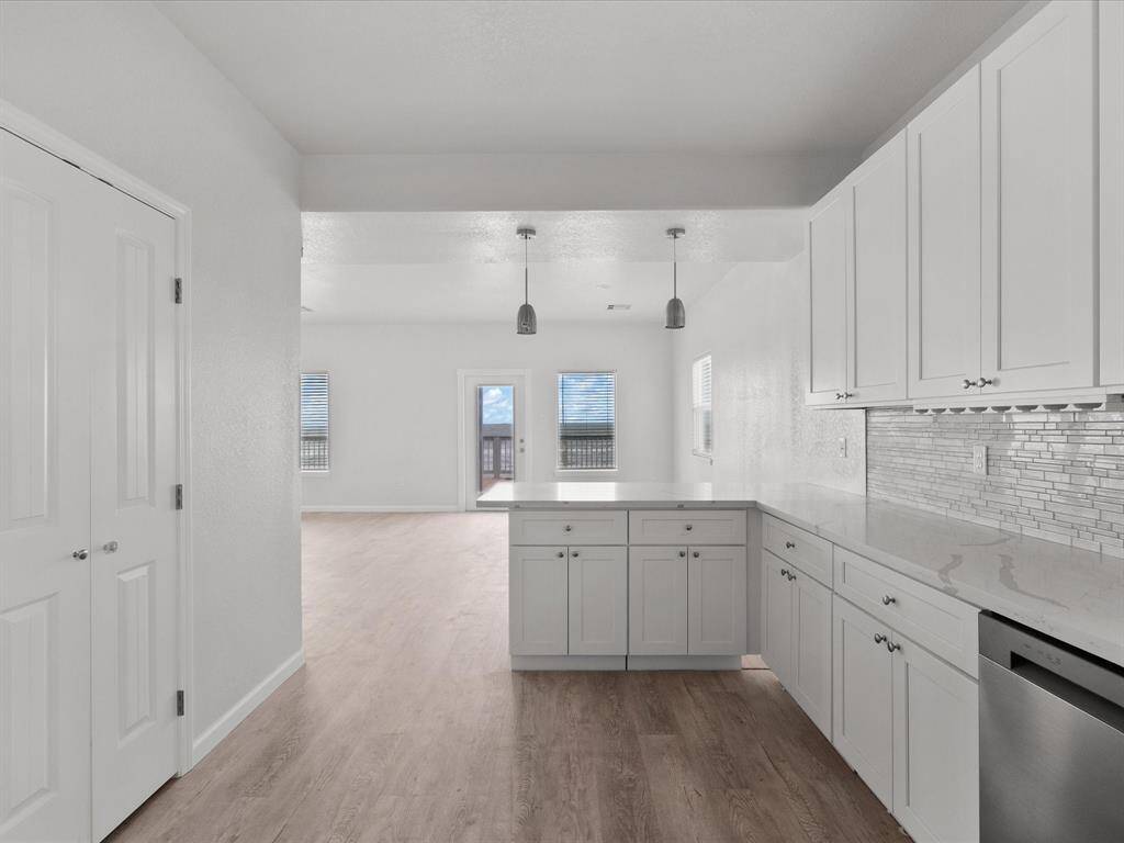 This photo showcases a modern, open-concept kitchen and living area. The kitchen features white cabinetry, a sleek backsplash, and stainless steel appliances, with ample natural light from large windows and a door leading to a deck. The space has light wood flooring and a neutral color palette, offering a bright and airy feel.