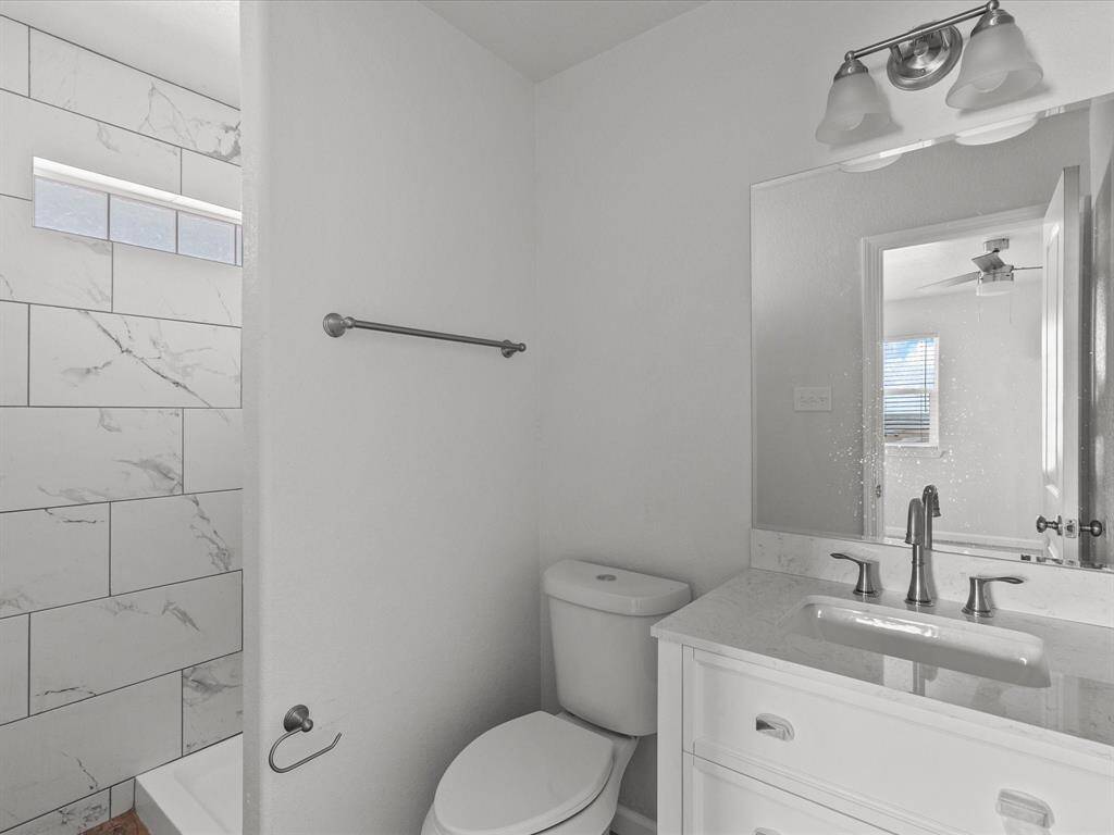 This bathroom features a modern design with a sleek white vanity, a large mirror, and a dual-light fixture. The shower has stylish marble-patterned tile, and the space is bright and clean.