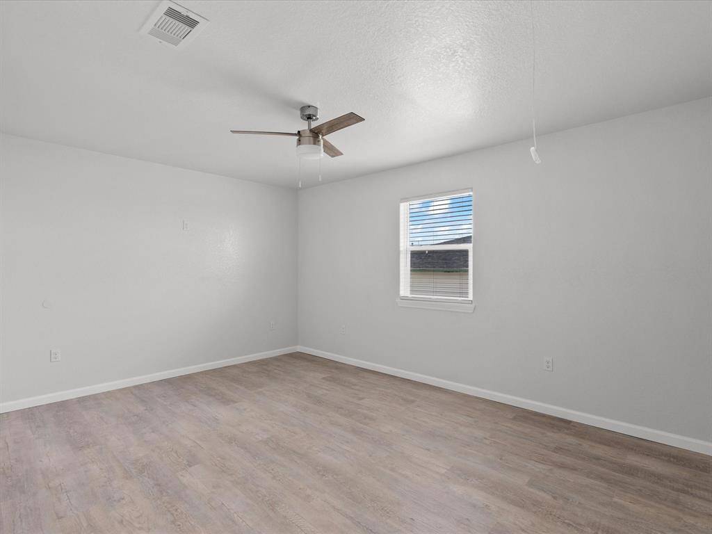 This room features freshly painted light gray walls, a modern ceiling fan, and a single window providing natural light. It has wood-style flooring and a simple, clean design.