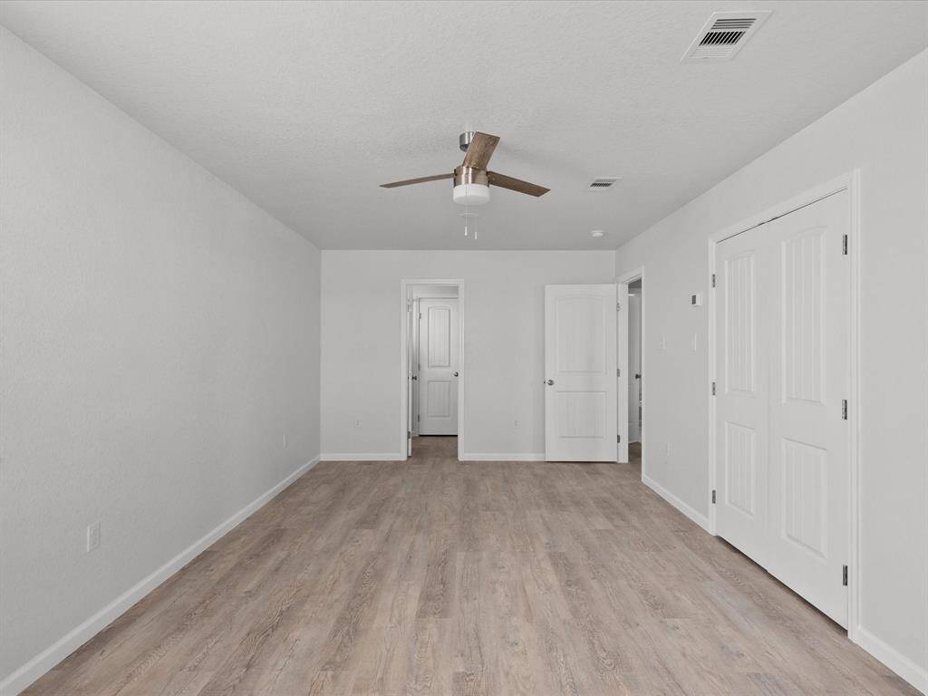This photo features a spacious, bright room with light gray walls and wood flooring. It includes a modern ceiling fan, double doors, and an additional doorway leading to another area. Perfect for a bedroom or office space.