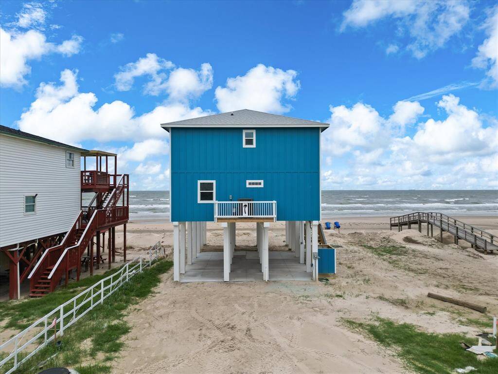 This photo shows a vibrant blue beachfront home elevated on stilts, offering direct access to the sandy beach and ocean views. Ideal for seaside living.