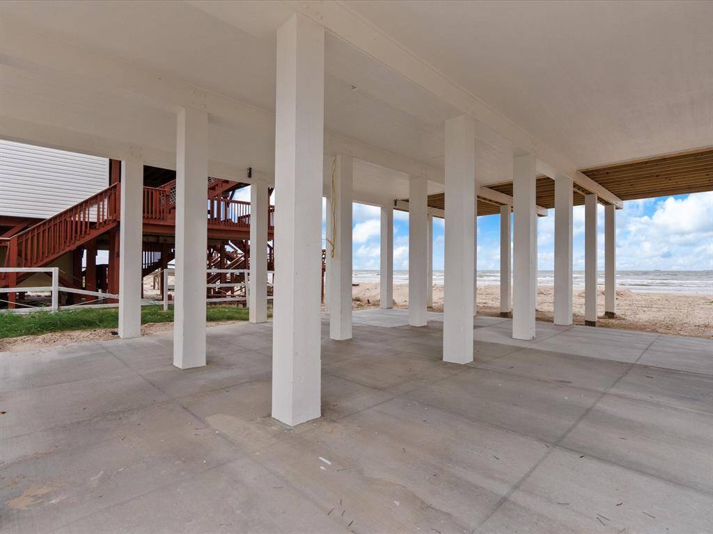 This photo shows an elevated beach house with concrete pillars providing open space underneath, offering direct access to sandy shores and ocean views. Ideal for coastal living.